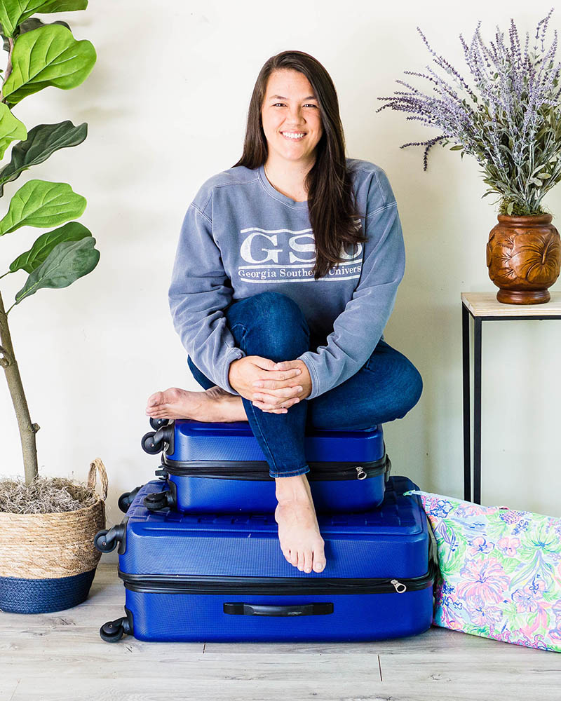 Savannah family photographer Jaden Giorgianni sits on a stack of blue suitcases