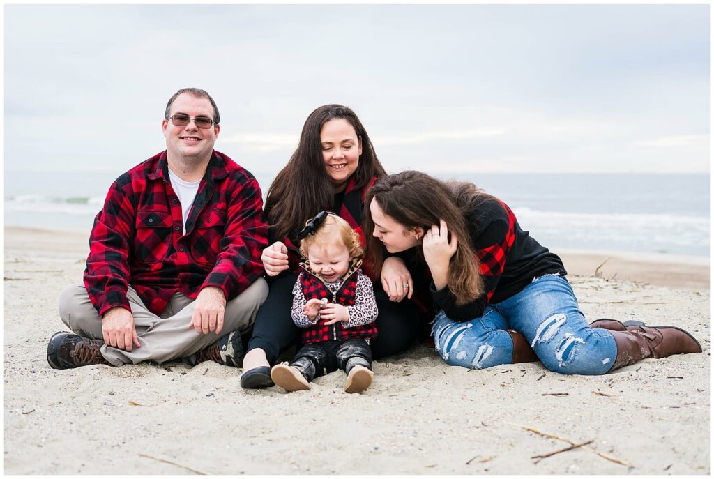 family sitting on beach wearing all red and black plaid