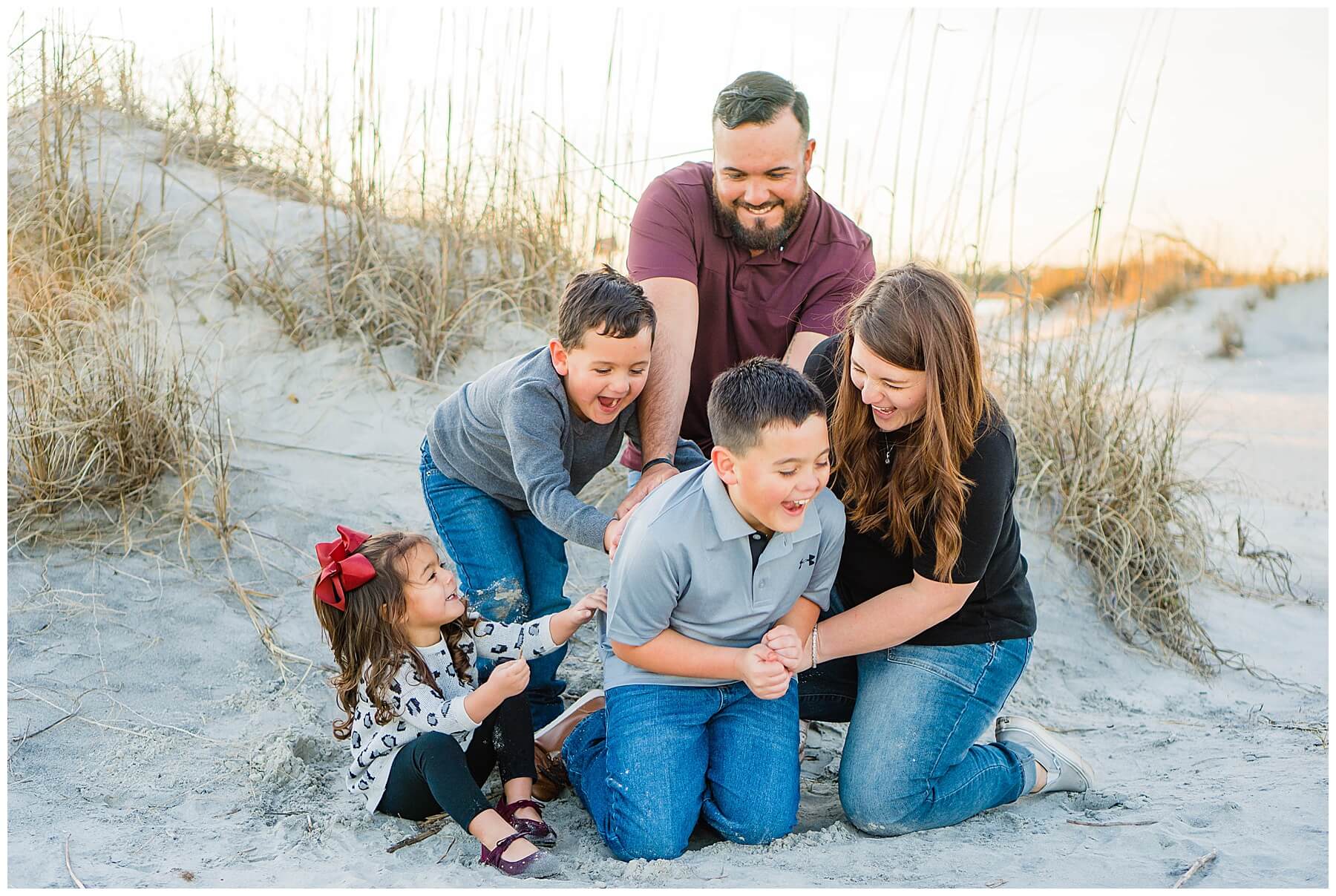 family of five tickling each other on the beach at sunset