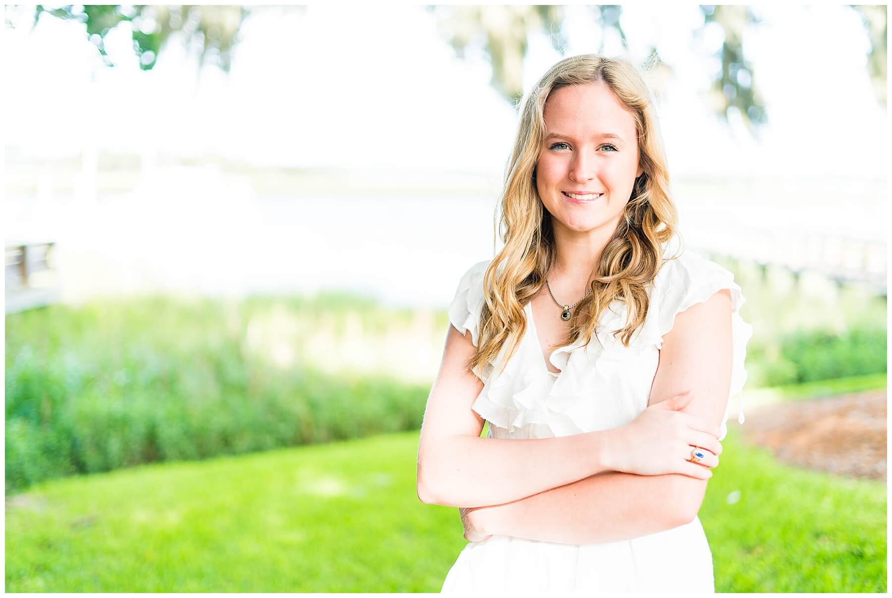 high school senior girl portrait in white romper standing in grass next to marina docks