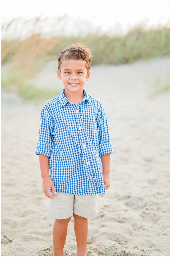 little boy in blue plaid shirt standing on Tybee Island Beach smiling at camera