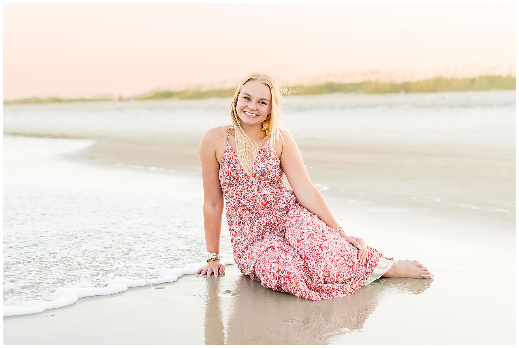 high school senior wearing a floral dress sitting in the surf on Tybee Island at sunset