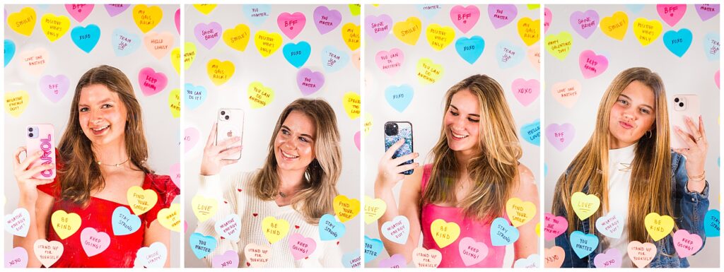 four high school girls standing in front of a mirror taking selfies with heart post it notes around the frame