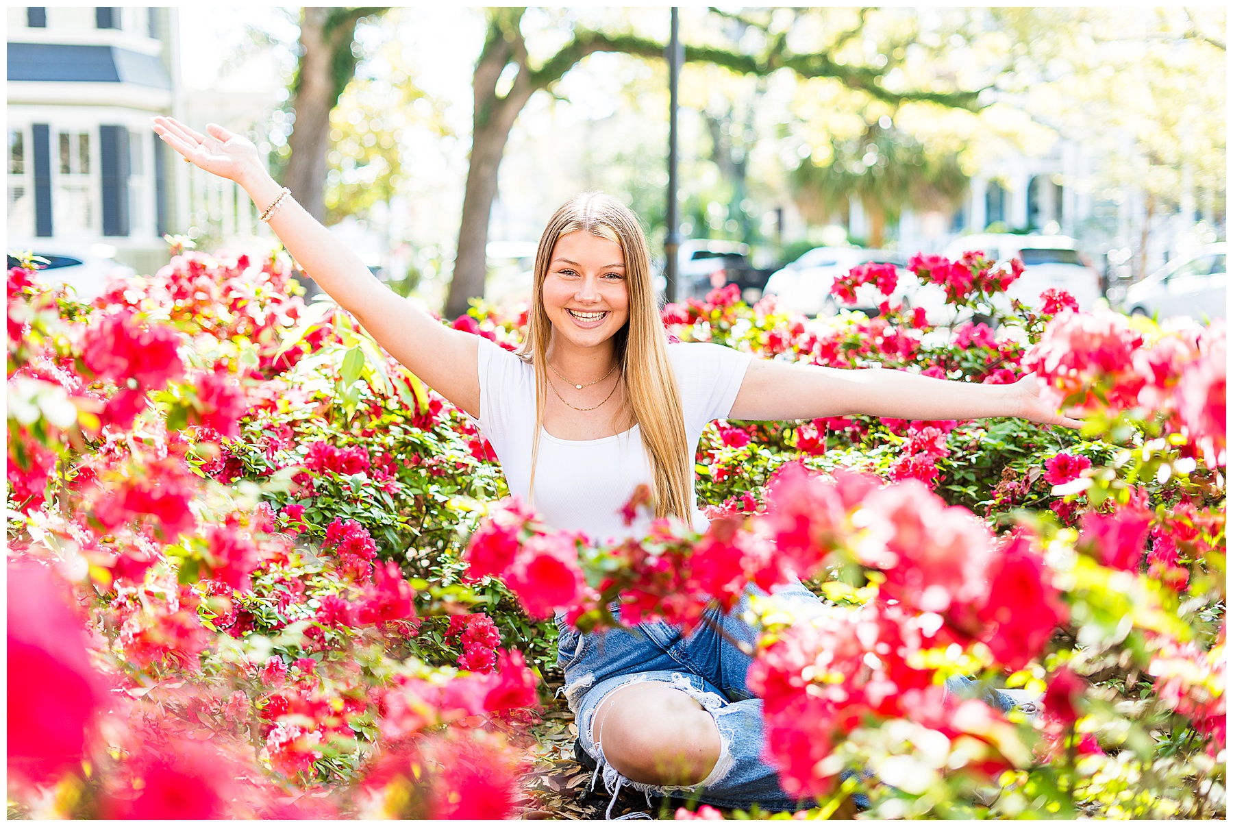 high school girl sitting in a bed of red azaleas in downtown Savannah's Whitefield square for senior pictures