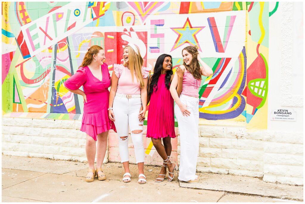 group of high school girls wearing various outfits in pink and white stand in front of a mural wall in downtown Savannah