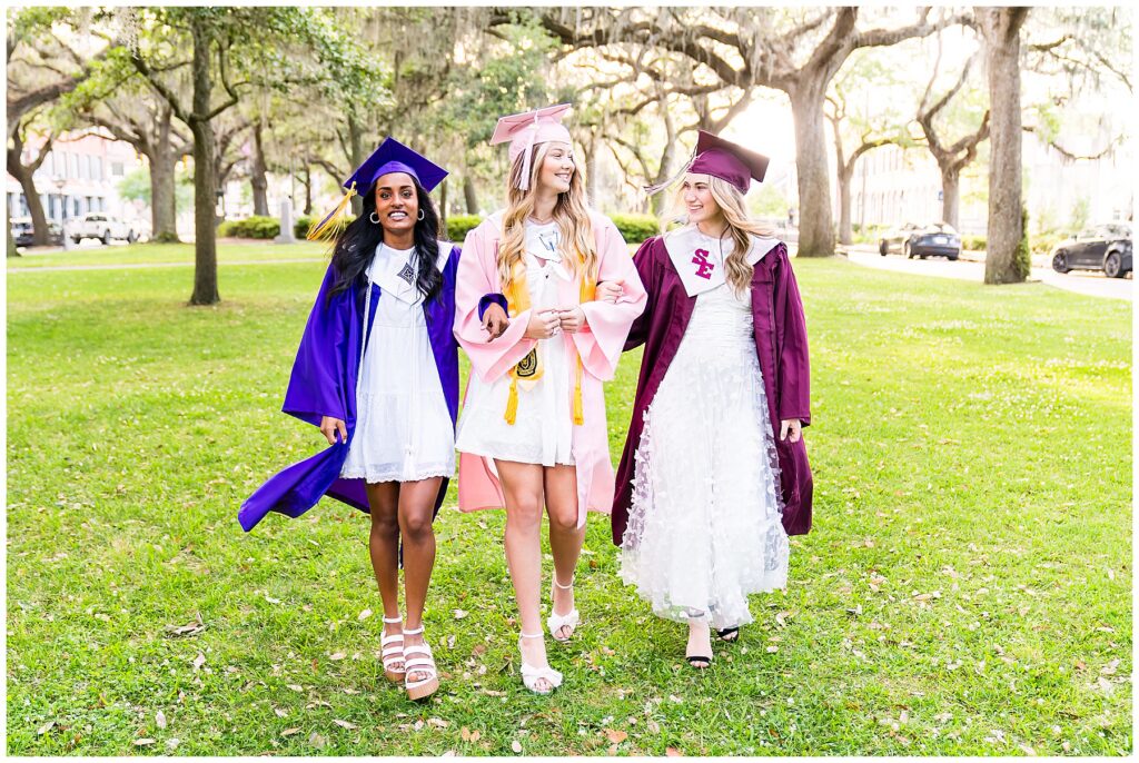 group of high school senior girls wearing cap and gowns and white dressed walking toward the camera laughing