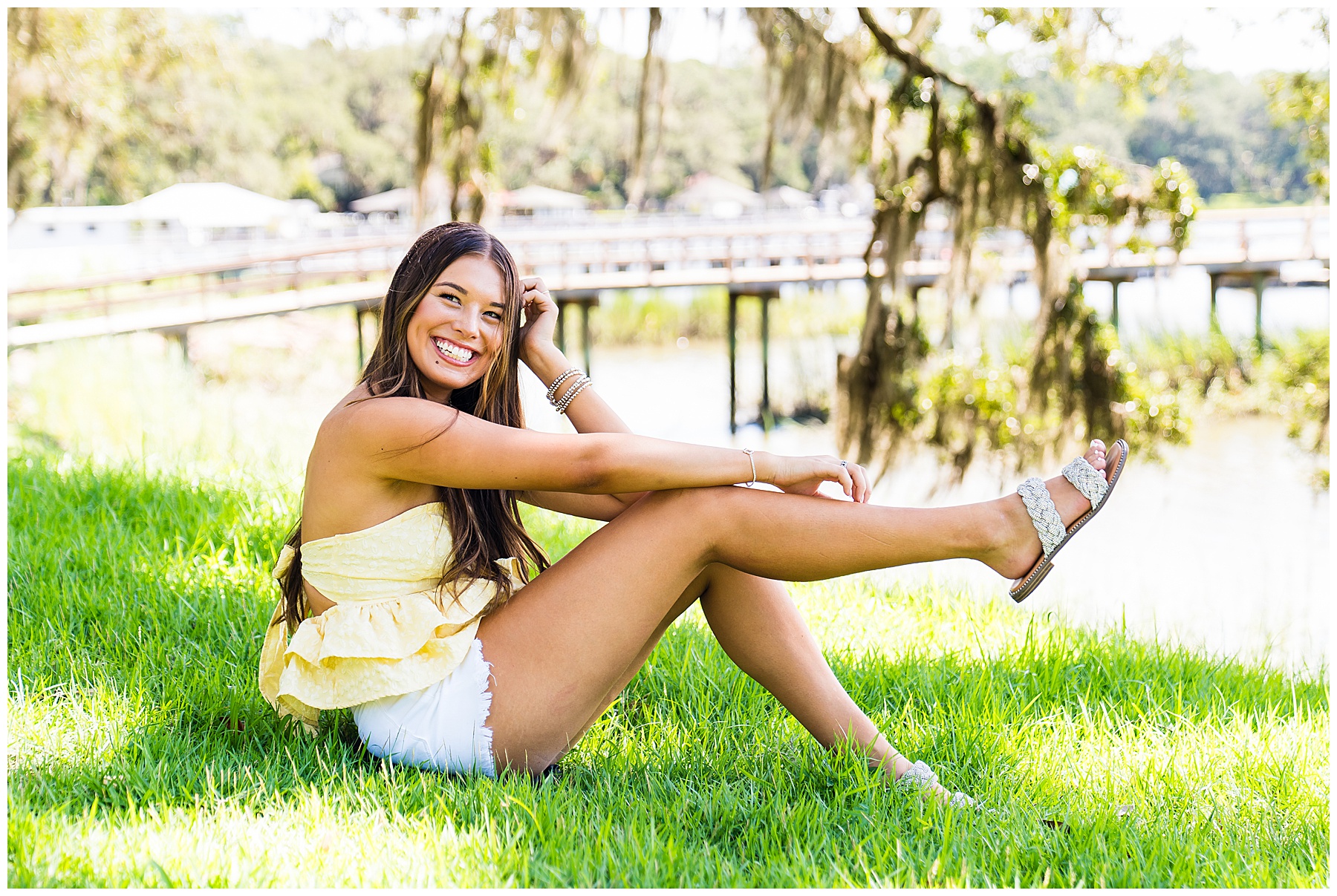 photo of a high school senior sitting in the grass wearing a yellow top and white shorts on bluff drive in savannah Georgia