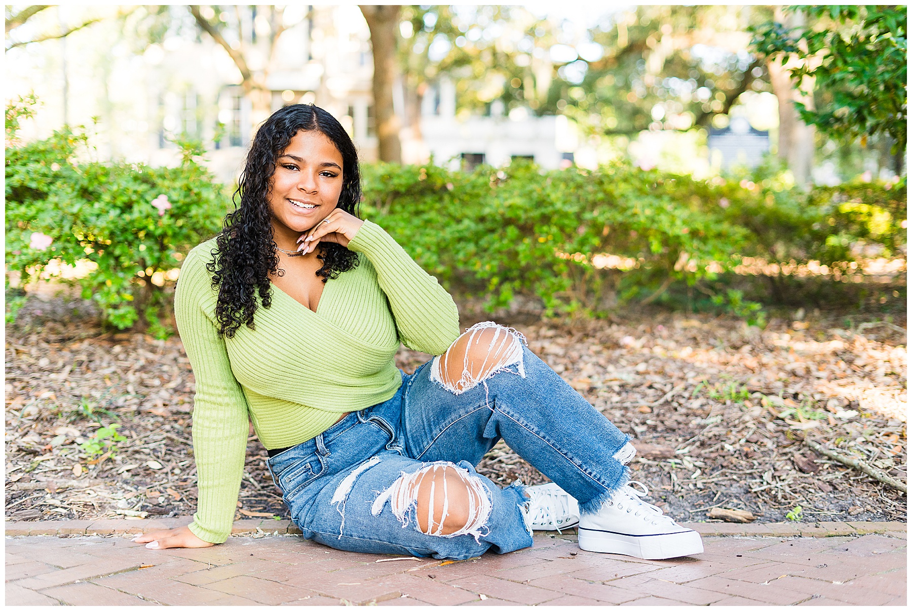 a high school senior wearing a green sweater with ripped blue jeans in downtown Savannah for senior pictures