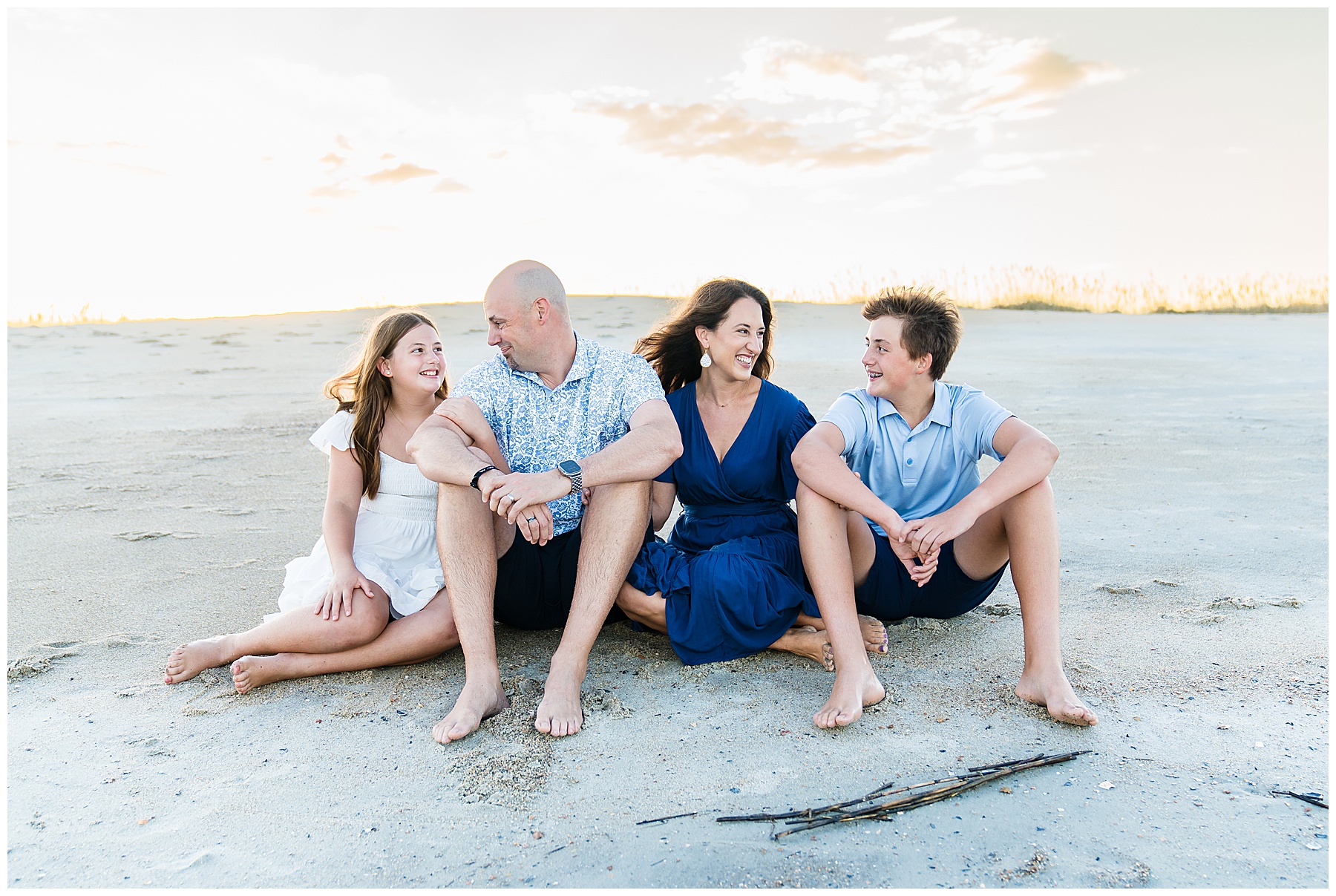 family of four sitting on the beach with the sun setting behind them