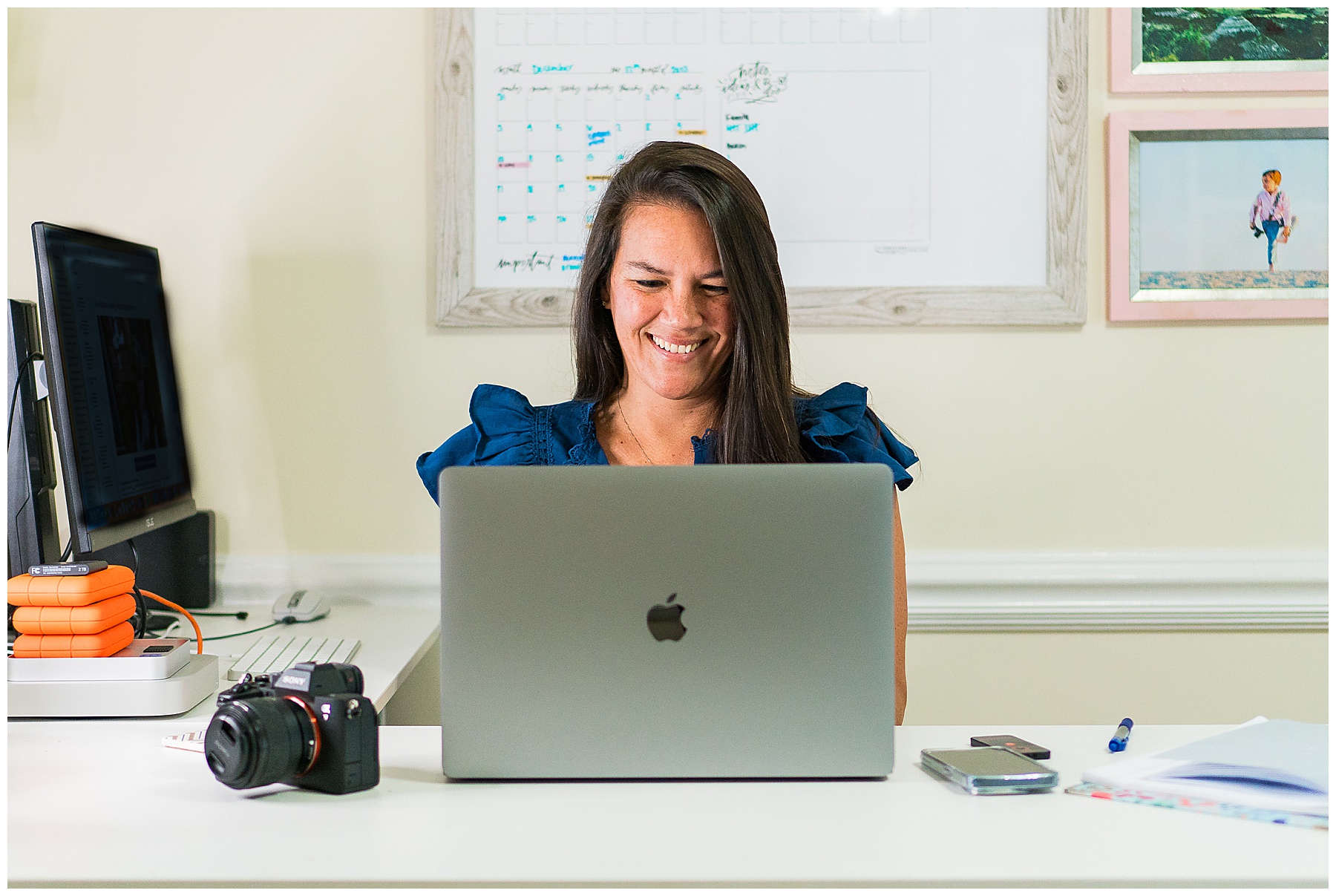 photographer wearing a dark blue shirt sitting at a desk typing on a laptop