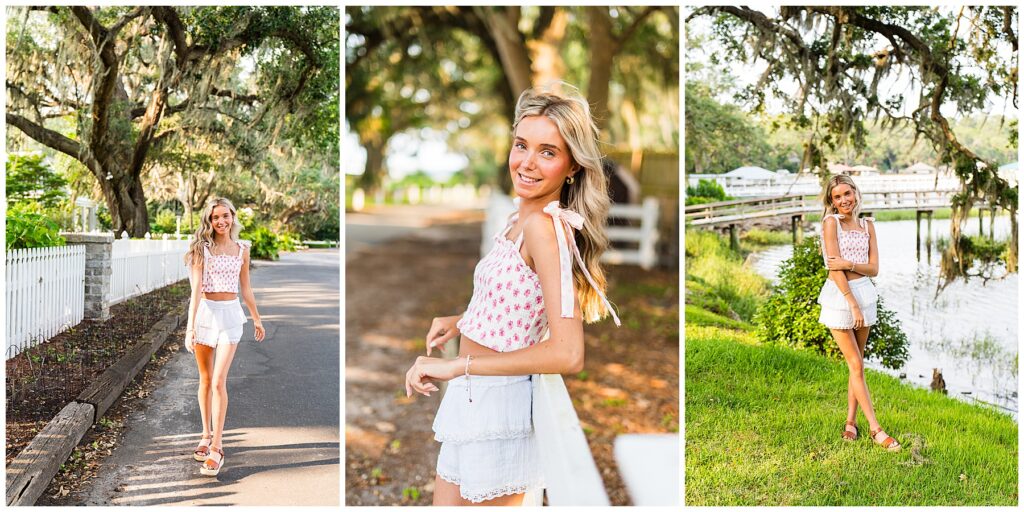 This collage features three golden-hour portraits of a high school senior in a bright and breezy summer outfit, set against scenic, Southern backdrops:

Left Image:
The senior is walking confidently down a shaded road lined with a white picket fence and moss-draped oak trees. She looks relaxed and happy, mid-step, as she smiles toward the camera. Her outfit consists of a smocked, pink floral tie-strap crop top and a tiered white mini skirt with lace trim. She wears brown platform sandals.
Center Image:
A close-up, side-angle portrait showing her soft curls, warm smile, and the delicate details of her top and jewelry. She stands beside a wooden fence with dappled sunlight filtering through the trees behind her, creating a dreamy, sunlit backdrop.
Right Image:
The senior poses near a peaceful waterfront, standing on lush grass with a boardwalk and boathouses visible in the background. Spanish moss drapes from the trees above, and she stands with one foot slightly crossed in front of the other, giving a soft, feminine stance.
Each image captures natural light beautifully and highlights her carefree, summery energy in different yet cohesive Lowcountry-inspired settings.